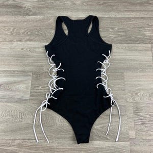 May include: Black tank top with white lace-up detailing on the sides. The top has a scoop neck and a racerback style.