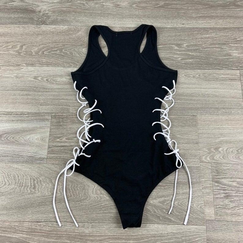May include: Black tank top with white lace-up detailing on the sides. The top has a scoop neck and a racerback style.