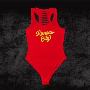 Może przedstawiać: Czerwony body z odkrytymi plecami i napisem "Kansas City" w ż&oacute;łtych literach.