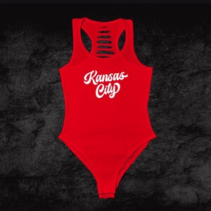 Może przedstawiać: Czerwony body z wycięciami na plecach i białym napisem "Kansas City" w stylu pisma odręcznego.