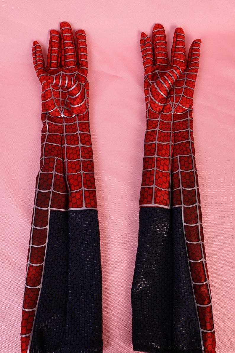 May include: A pair of long, elbow-length gloves featuring a red fabric base with a black spiderweb pattern printed in silver lines. The lower section of each glove is solid black with a textured, grid-like surface pattern throughout the material.