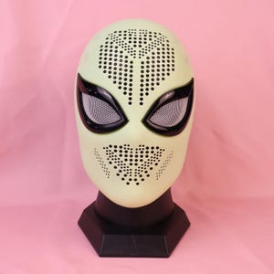 May include: A pale green full-head mask featuring a perforated dot pattern across the forehead and mouth area. The mask includes two large, almond-shaped eye openings framed in black with white mesh lenses, all displayed on a black stand.