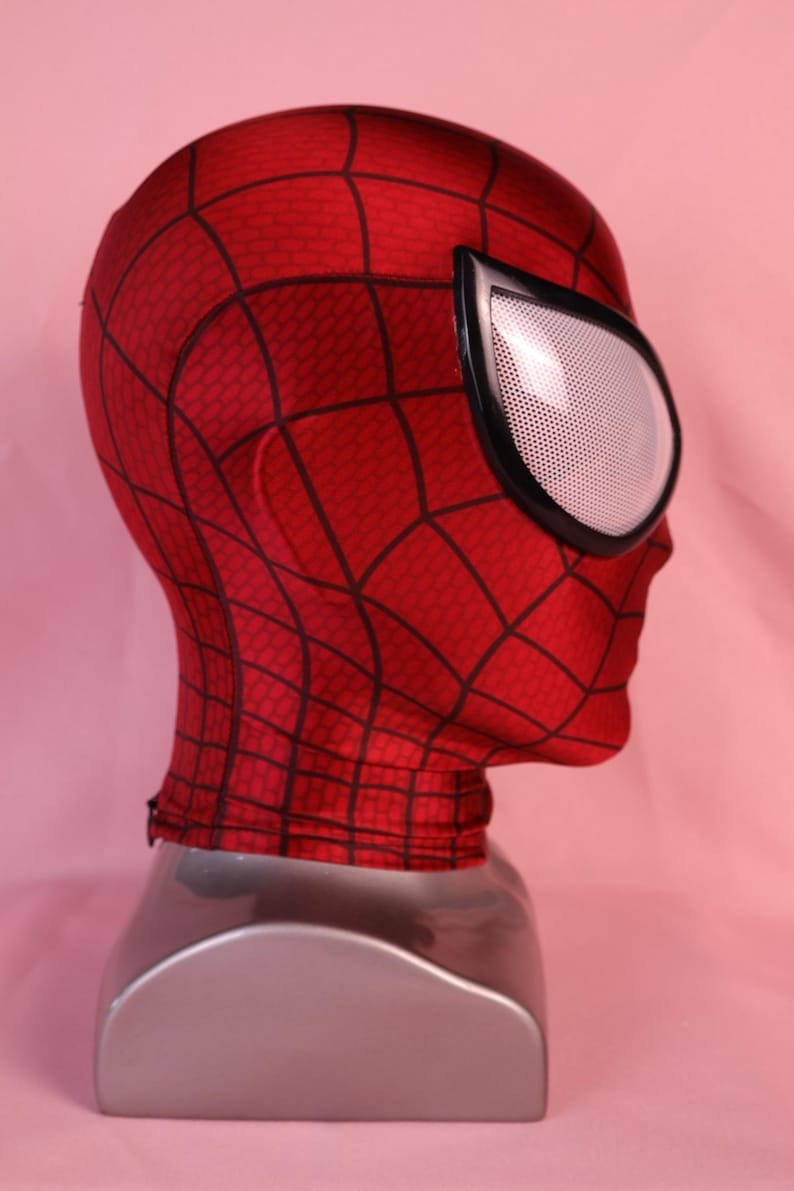 Pode incluir: Uma m&aacute;scara de tecido vermelho com um padr&atilde;o de teia de aranha preta em toda a superf&iacute;cie. A m&aacute;scara inclui lentes oculares grandes em forma de am&ecirc;ndoa com uma textura de malha branca e uma borda preta espessa, cobrindo cabe&ccedil;a e pesco&ccedil;o.