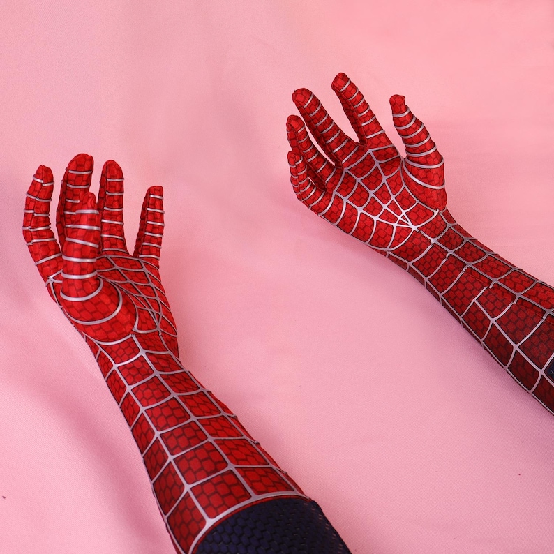 May include: A pair of long, red fabric gloves featuring a silver web pattern across the fingers, palms, and forearms. The gloves extend past the wrists and are constructed from a textured material with a distinct grid-like design throughout.