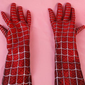 May include: A pair of long, red gloves featuring a printed silver web pattern that covers the entire surface. The gloves extend past the wrist and are designed with individual finger sections, showcasing a detailed grid-like texture throughout.