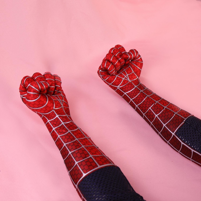 May include: A pair of red and blue fabric sleeves featuring a printed silver spiderweb pattern. The sleeves cover the arms and hands, ending in clenched fists, with a textured blue fabric section visible at the lower forearm area of each sleeve.