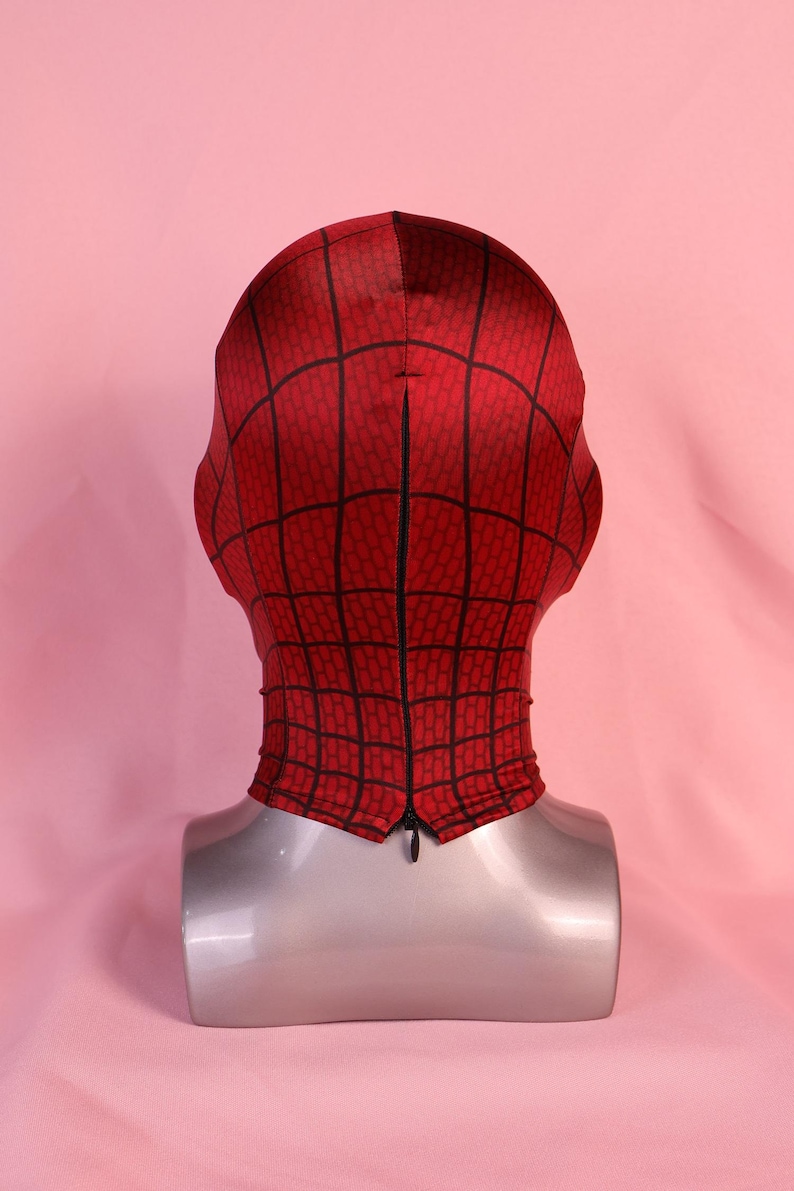 Pode incluir: Uma m&aacute;scara de tecido vermelho com um padr&atilde;o de teia de aranha preta impresso na superf&iacute;cie. A m&aacute;scara &eacute; exibida num manequim de cabe&ccedil;a e pesco&ccedil;o prateado, com um fecho de correr preto vertical ao longo do centro da parte traseira.