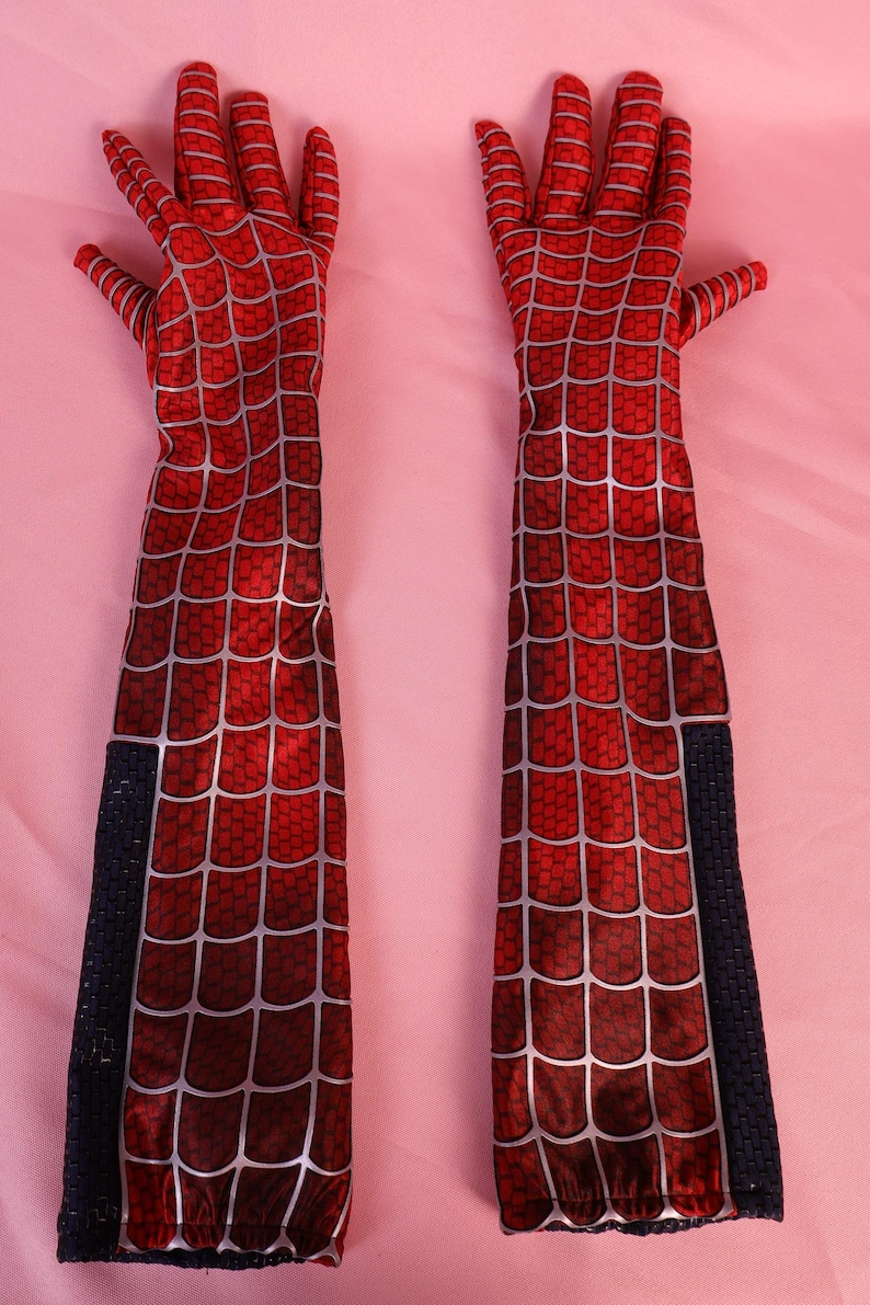 May include: A pair of long, elbow-length gloves featuring a vibrant red fabric base with a printed silver web pattern. The gloves have a textured appearance and include a vertical black panel along the outer forearm of each piece.