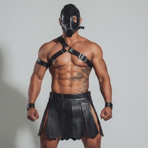 Könnte beinhalten: Eine Person trägt eine schwarze Gasmaske, einen schwarzen Ledergurt und einen schwarzen Lederrock. Der Rock hat Falten und Seitenschlitze. Die Person steht vor einem schlichten weißen Hintergrund.