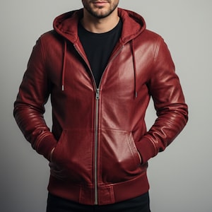Op de afbeelding: Bordeaux leren jack met capuchon, volledige ritssluiting en voorzakken. De jas heeft geribde manchetten en een geribde zoom. Het model draagt er een zwart t-shirt onder.