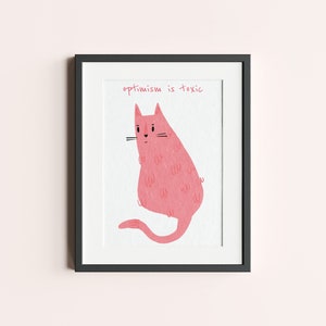 Può includere: Una stampa incorniciata con un'illustrazione di un gatto rosa e il testo "l'ottimismo è tossico".