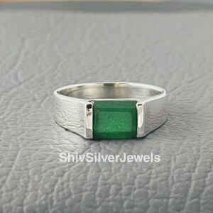 May include: A silver ring with a square green gemstone. The ring has a simple design and is a classic style.