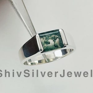 May include: A silver ring with a green moss agate stone. The ring is set in a simple band with a square-shaped stone.