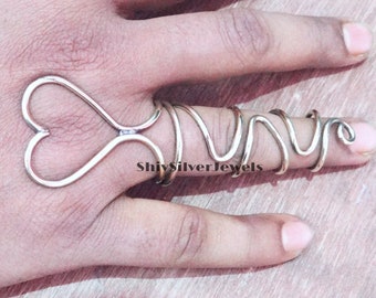 May include: A silver heart-shaped ring and a silver spiral ring worn on a finger.