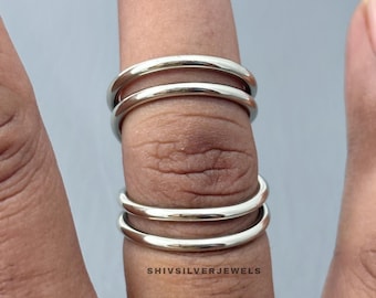 May include: A silver ring with three stacked bands is worn on a finger. The bands are smooth and shiny. The ring is shown against a gray background. The text "SHIVSILVERJEWELS" is visible.