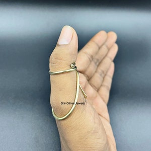 May include: A gold thumb ring with a twisted design. The ring is worn on the thumb of a hand.