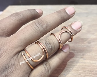 May include: A set of three copper wire rings, stacked on a finger. The rings are all different sizes and shapes, and they are all made of a single piece of wire. The rings are a warm copper color.