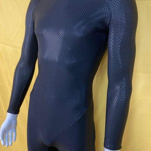 May include: A black, long-sleeved bodysuit with a textured, woven pattern. The garment has a crew neck and a form-fitting design. The fabric appears to be a dark, solid color, and the bodysuit is displayed on a mannequin.