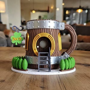 Könnte beinhalten: Ein skurriles, braunes und goldenes Dekorationsstück im Pub-Stil. Das Design umfasst eine Tür, eine Leiter und ein grünes Kleeblatt-Schild mit der Aufschrift "PUB". Das Objekt ist von grünen Büschen umgeben und hat ein Metallband am oberen Rand.
