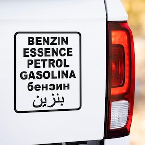 Könnte beinhalten: Ein weißer LKW mit einem schwarzen Aufkleber auf der Rückseite, auf dem in verschiedenen Sprachen "BENZIN ESSENCE PETROL GASOLINA бензин بنزين" steht.