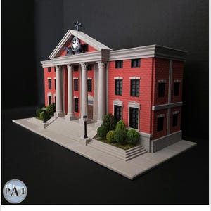 May include: A miniature model of a red brick courthouse with white columns, a clock tower, and a cross on top. The model has a gray base with small green bushes and a black background. The courthouse has multiple windows and a front door.
