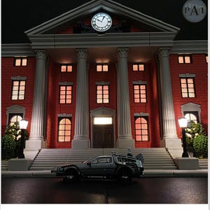 May include: A miniature model of a red brick building with white columns and a clock, illuminated by warm lighting. A silver DeLorean car is parked in front of the building, creating a scene reminiscent of a movie.