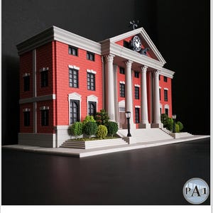 May include: A miniature model of a red brick courthouse with white columns and a clock tower. The building has multiple windows and a small garden in front. The model is set against a dark background.