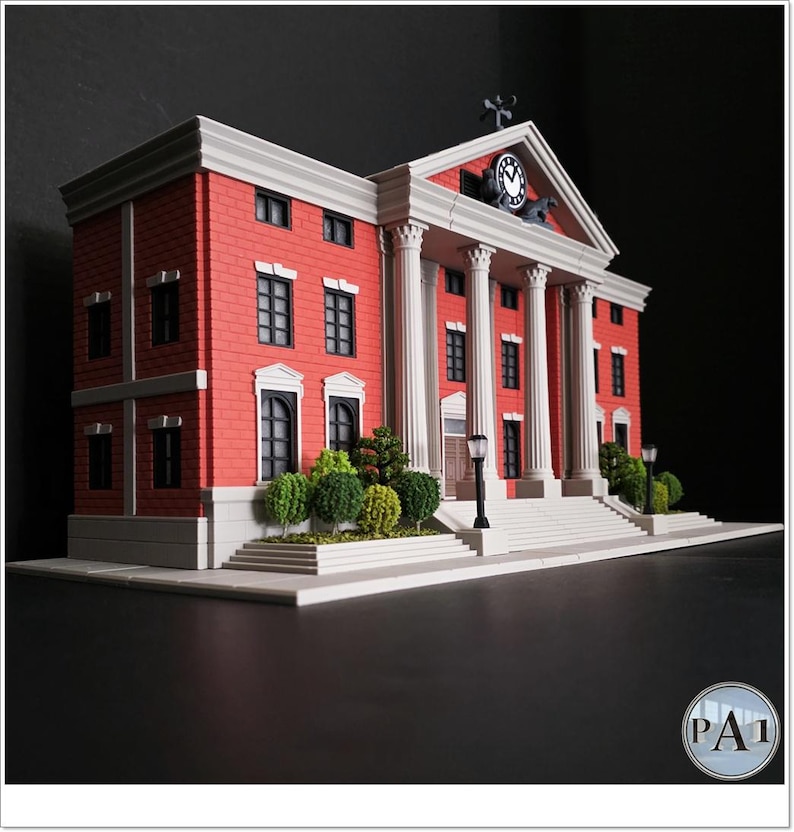 May include: A miniature model of a red brick courthouse with white columns and a clock tower. The building has multiple windows and a small garden in front. The model is set against a dark background.