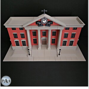 May include: A detailed model of a brick building with white columns, a clock, and a cross on top. The building has multiple windows and a light gray base. The model is a replica of a courthouse.