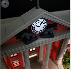 May include: A detailed model of a building with a clock tower. The clock face is illuminated, showing Roman numerals. The building has a red brick facade, white columns, and two black statues. The overall design is intricate and detailed.