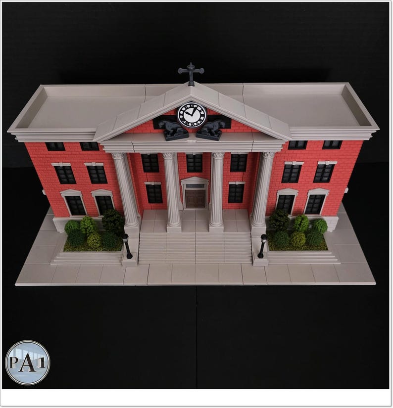 May include: A detailed model of a red brick building with white columns, a clock, and a cross on top. The building has multiple windows and a gray roof. The model includes a base with greenery and street lamps.