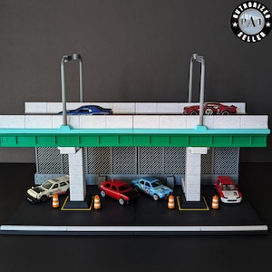 May include: A miniature diorama of a parking garage with several toy cars. The garage has a green and white structure with two levels, and includes miniature traffic cones and street lights. The cars are various colors, including red, blue, and white.