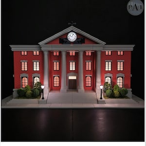 May include: A miniature replica of a red brick building with white columns and a clock tower. The building has multiple windows with interior lighting, and small bushes and street lamps are in front. The clock shows the time.