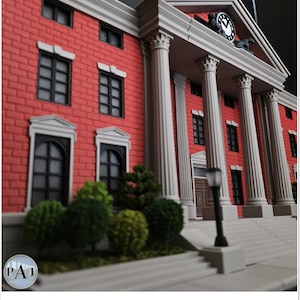 May include: A miniature model of a red brick building with white columns and a clock tower. The building has black windows and doors, with green shrubbery in front. The clock tower has a clock face and two horse figures.