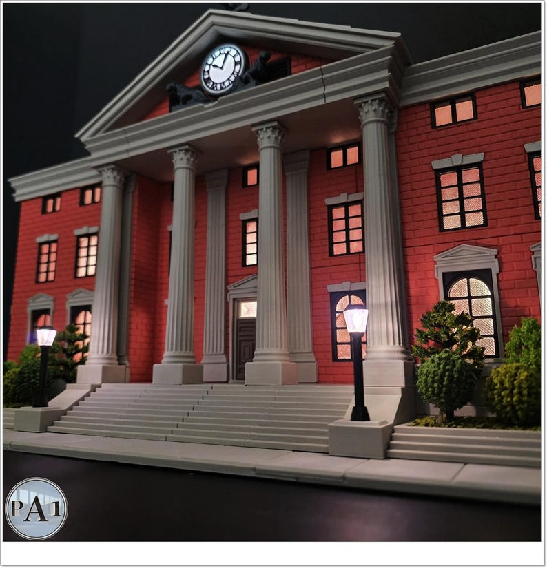 May include: A detailed model of a red brick building with white columns and a clock tower. The building has multiple windows with interior lighting, and is flanked by street lamps and greenery. The clock shows the time.
