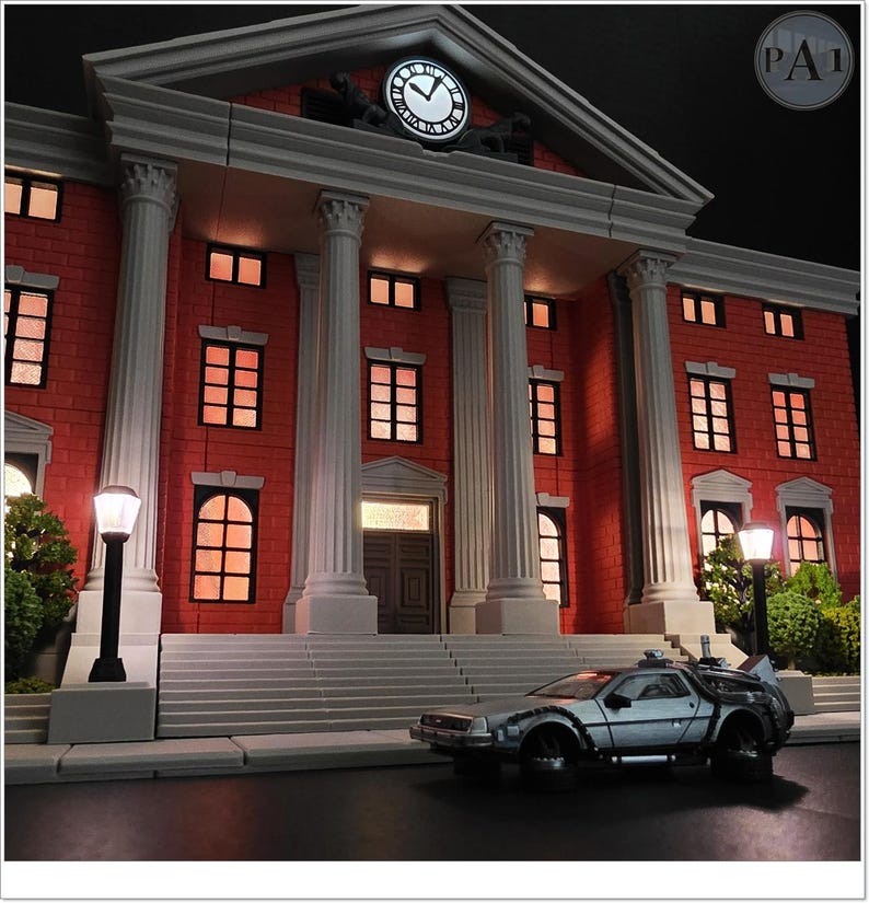 May include: A detailed model of the Hill Valley Courthouse from Back to the Future, featuring a glowing clock tower and a silver DeLorean time machine. The building is red brick with white columns and windows. The scene is set at night.