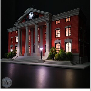 May include: A miniature model of a red brick building with white columns and a clock tower. The building has multiple windows with interior lighting, and is flanked by small trees and street lamps. The model is set against a dark background.