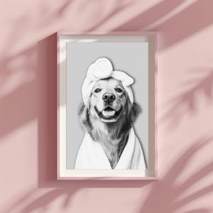 May include: A framed wall art print featuring a black and white portrait of a golden retriever dog wearing a white towel wrapped around its head and a white bathrobe. The dog is centered against a solid light gray background within a pink frame.