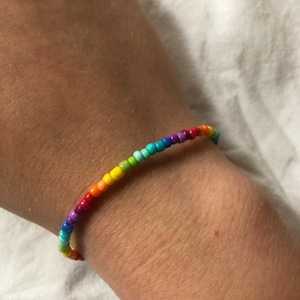 Könnte beinhalten: Ein Regenbogen-Armband mit kleinen, runden Perlen in verschiedenen Farben, darunter Rot, Orange, Gelb, Grün, Blau, Indigo und Violett.