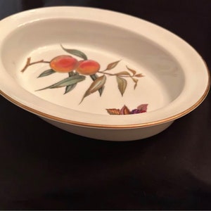 Puede incluir: Un plato para hornear ovalado blanco con un borde dorado y un diseño de melocotón y hojas.