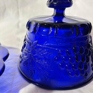 K&ouml;nnte beinhalten: Eine Butterschale aus kobaltblauem Glas mit Deckel. Die Schale ist mit einem Traubenranken- und Traubenmuster verziert.