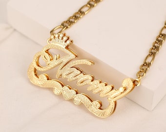Può includere: Collana d'oro con un ciondolo a placca con nome in corsivo che dice "Mommy" con una piccola corona sopra la prima lettera e tre piccoli cuori sotto il nome. La collana ha una catena a curb d'oro.