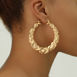 May include: Gold hoop earrings with a textured, woven design. The earrings are large and have a circular shape.