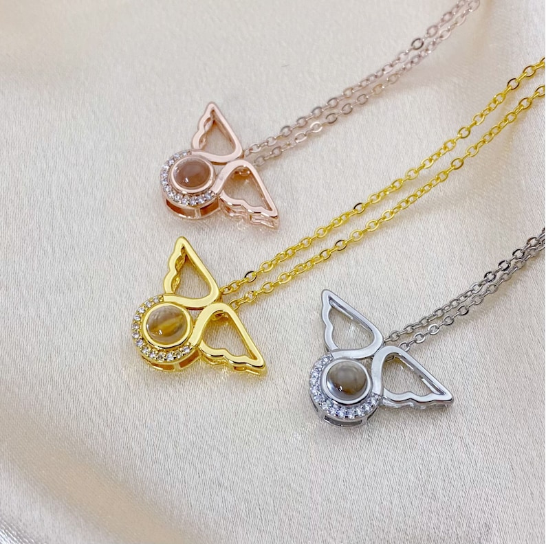 May include: Three silver angel wing necklaces with a clear crystal in the center of each pendant. The necklaces are on a white background.
