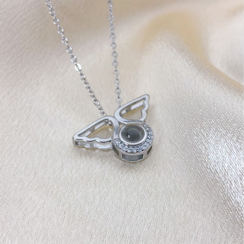May include: Silver angel wing necklace with a small round pendant that projects an image when viewed through a light source.