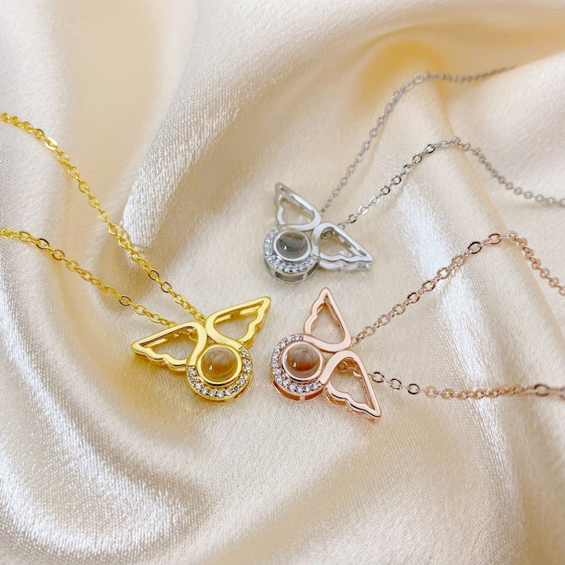 May include: Three angel wing necklaces with a small round stone in the center. The necklaces are gold, silver, and rose gold.