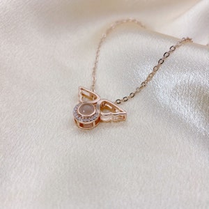 May include: A rose gold necklace with a small angel pendant featuring a clear stone surrounded by smaller stones. The angel has delicate wings.