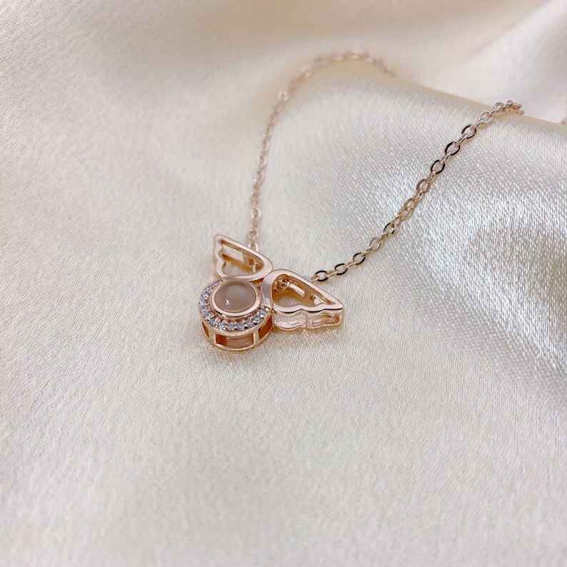 May include: A rose gold necklace with a small angel pendant featuring a clear stone surrounded by smaller stones. The angel has delicate wings.