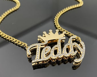 May include: Gold chain necklace with a gold pendant featuring the name "Teddy" in cursive script with rhinestones and a gold crown on top.