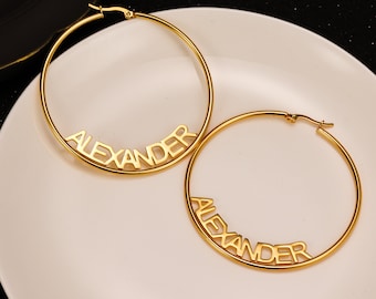May include: A pair of gold hoop earrings with the name "ALEXANDER" spelled out on each earring.